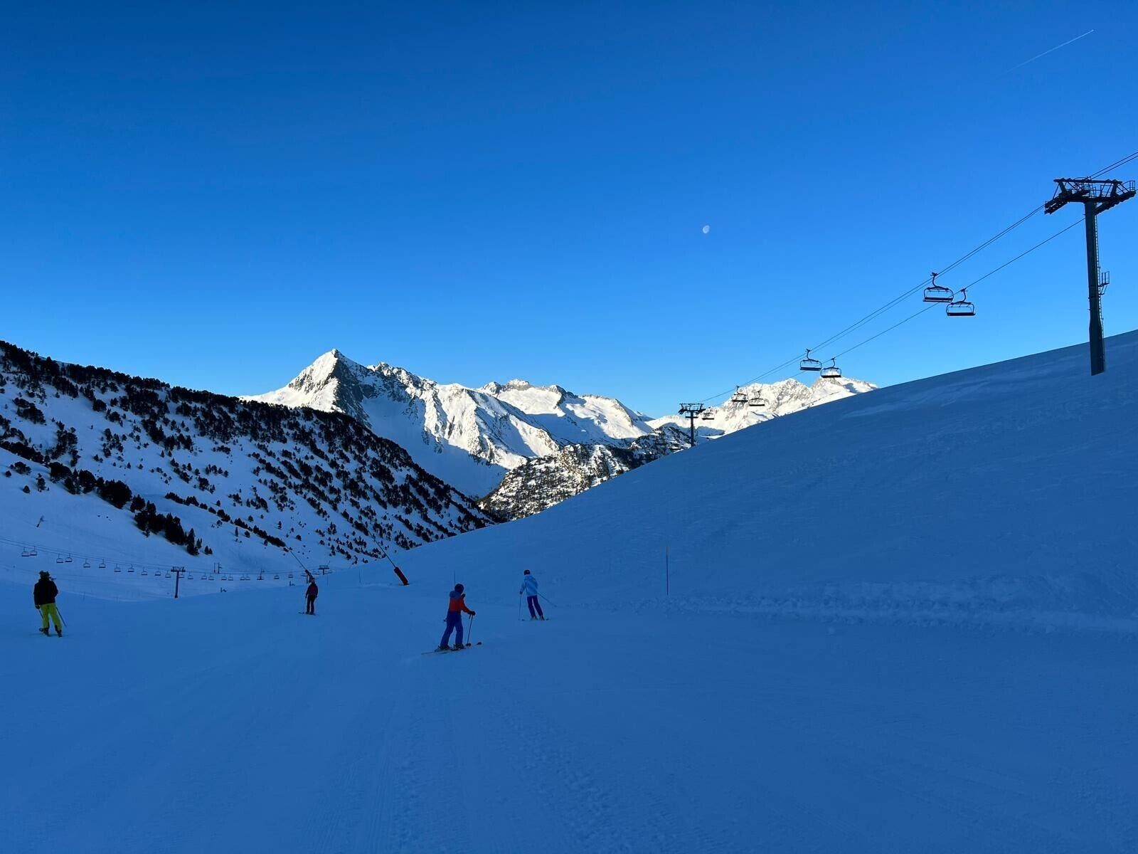 Een besneeuwde helling met skiërs, een skilift en een helderblauwe lucht.