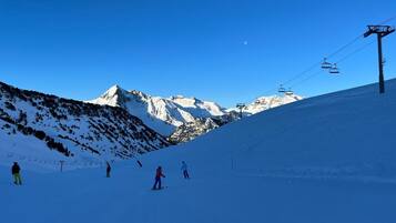 Een besneeuwde helling met skiërs, een skilift en een helderblauwe lucht.