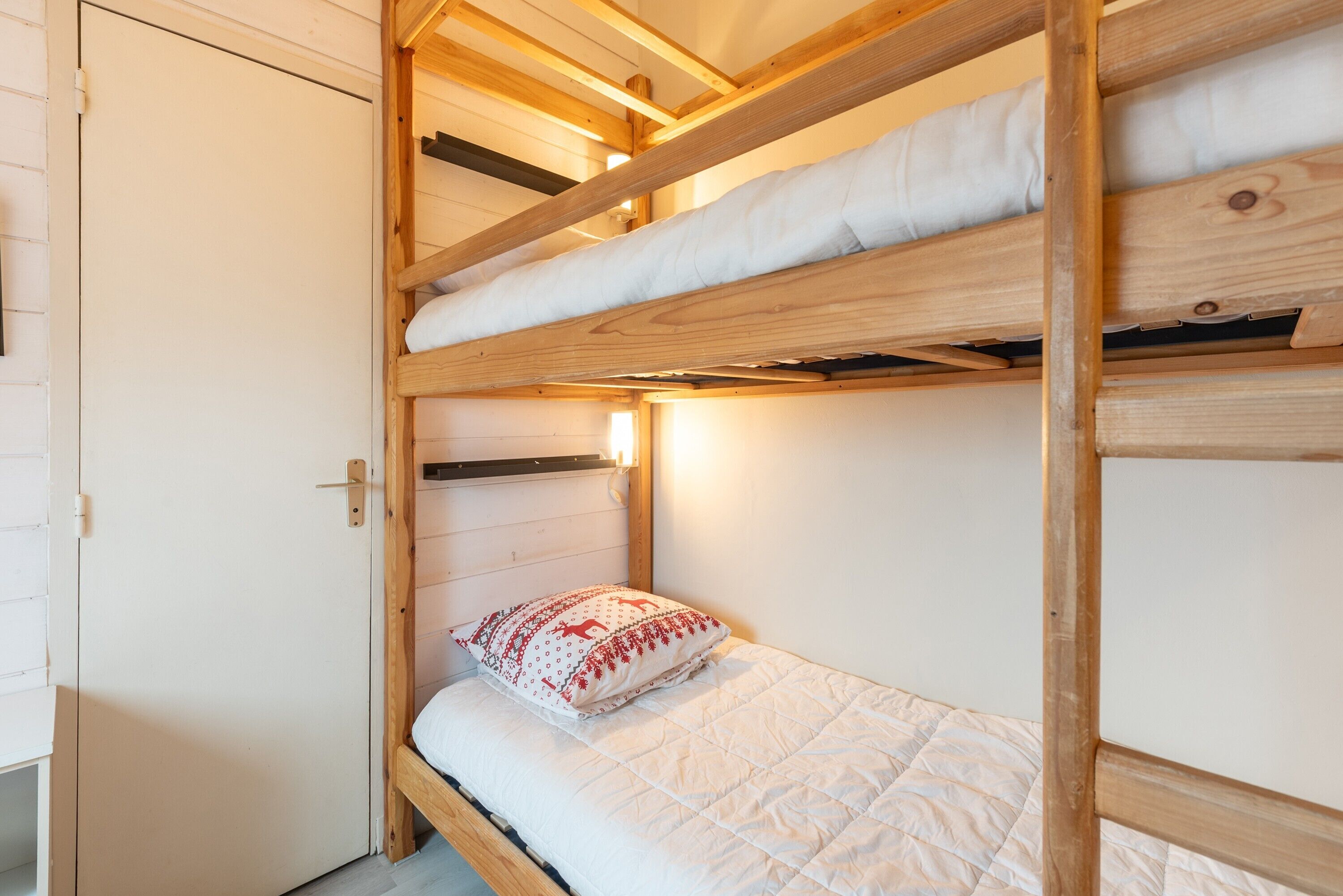 Un lit superposé avec une structure en bois, un matelas blanc et un coussin décoratif.