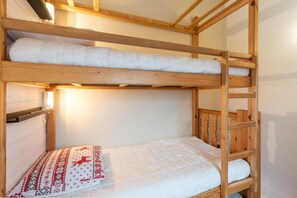 Uma beliche com uma cama de baixo e uma cama de solteiro, ambas com roupa de cama branca.