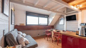 A cozy cabin interior with a sofa, dining table, chairs, a kitchen area, and a TV.