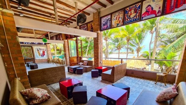 A cozy lounge area with cushioned seating, a stage, and a large window with a view of palm trees. - Hotel Boutique el Mirador  (Arboletes)