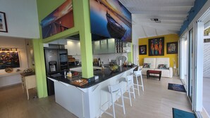 A modern kitchen with a central island, white bar stools, and a dining area with a sofa and chairs. - Villa AMAYA for 4 people (Saint-François)