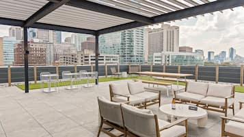 An outdoor patio with seating and tables, overlooking a cityscape with high-rise buildings.