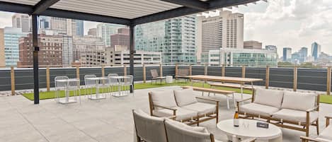 An outdoor patio with seating and tables, overlooking a cityscape with high-rise buildings.