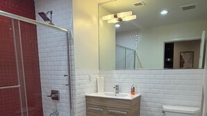 Ein modernes Badezimmer mit einer Duschkabine aus Glas, einem weißen Waschbecken mit Holzschrank und einer Toilette.