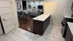Eine moderne Küche mit einer zentralen Kochinsel, weißen Fliesenböden und einem Essbereich mit einer Couch und Tisch.