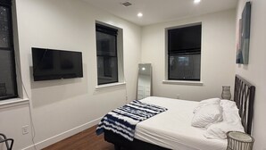 Ein modernes Schlafzimmer mit einem großen Bett, einem Flachbildfernseher und einem Nachttisch mit einer Vase.