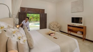 A bedroom with a bed, a TV, a chair, and a door leading to an outdoor area. - Villa Kubu Seminyak (Bali)