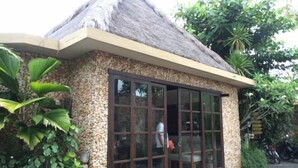A small building with a thatched roof, large glass windows, and a stone exterior. - Villa Kubu Seminyak (Bali)