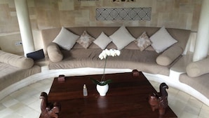 A living room with a dark wooden coffee table, a white vase with a plant, and a beige sofa with patterned cushions. - Villa Kubu Seminyak (Bali)