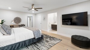 Ein modernes Schlafzimmer mit Bett, Schreibtisch, Fernseher und einem durchgegangenen Tür erkennbaren Badezimmer.