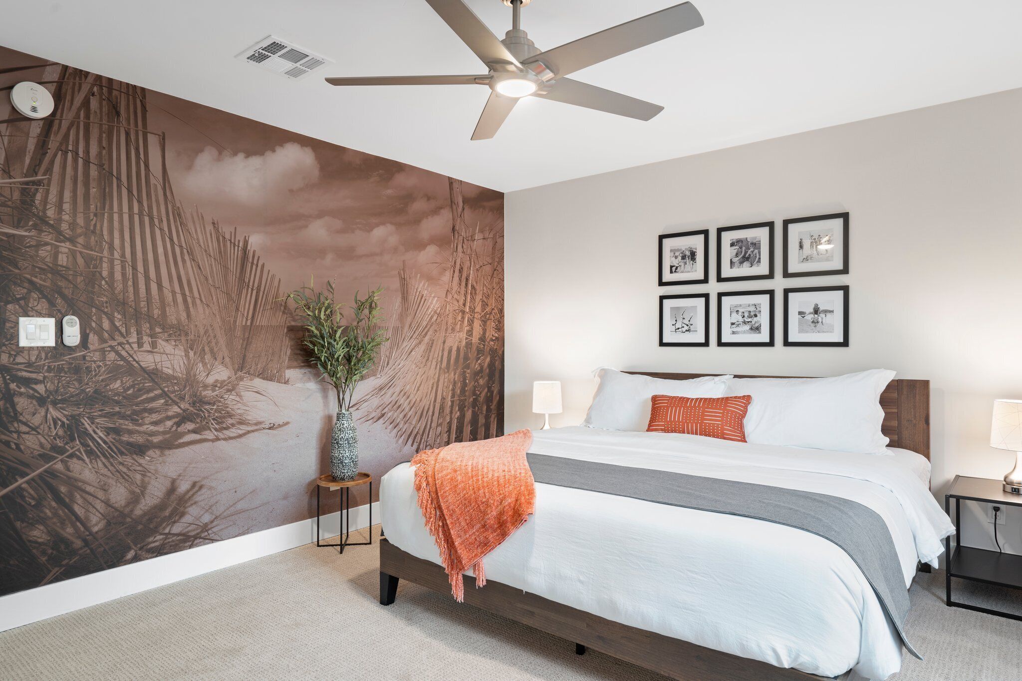 A bedroom with a large bed, a ceiling fan, a wall mural, and framed pictures.