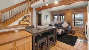 A spacious living area with a wooden staircase, a dining table with bar stools, and a cozy seating area with a sofa and cushions.