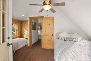 A bedroom with two beds, a wooden door, a ceiling fan, and a window.