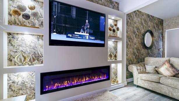 Een moderne woonkamer met een flatscreen televisie aan de muur, decoratieve muurkunst, een open haard en een comfortabele bank.