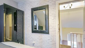 Een slaapkamer met een bed, een grote spiegel, een witte bakstenen muur en een deur naar een balkon.