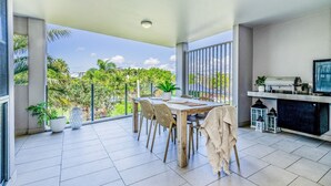 A modern dining area with a view of greenery, a fireplace, and a television. - Pavillions  Ocean Breeze Apartment 119 (Agnes Water)