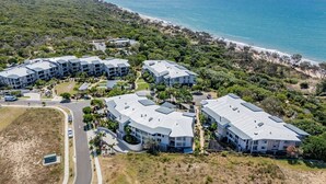 A coastal resort with multiple buildings featuring flat roofs and balconies, surrounded by lush greenery and a beach. - Pavillions  Ocean Breeze Apartment 119 (Agnes Water)