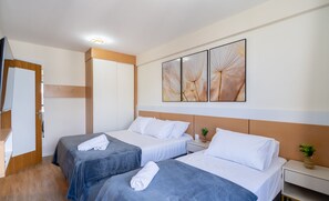 A hotel room with two beds, a wooden wardrobe, a bedside table with a plant, and a wall with three framed artworks. - Fully Equipped Accommodations in a Building With Pool and gym in Downtown Florianopolis - Lins (Florianópolis)