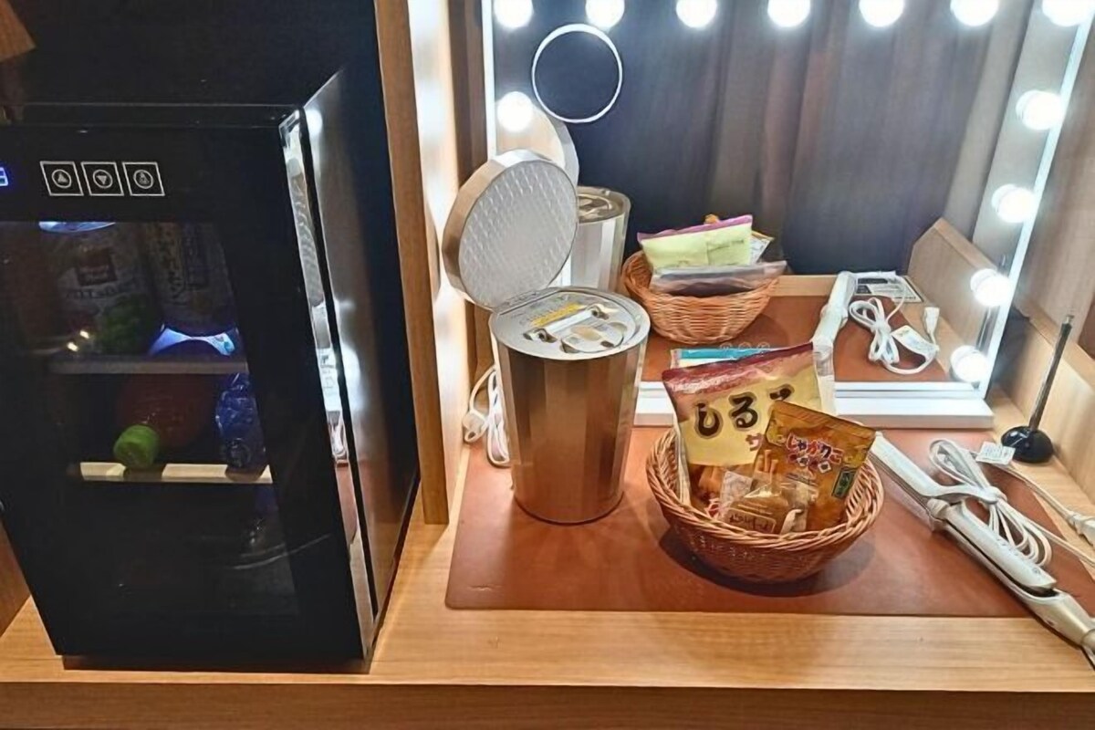 Een compacte koelkast met een digitaal display, een magnetron, een mand met snacks en een make-upspiegel met verlichting.