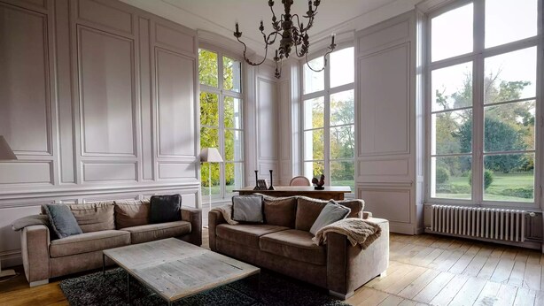 Una habitación amplia con dos sofás, una mesa de centro y un radiador. Amplias ventanas ofrecen vistas al exterior.