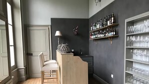 Una habitación con piso de madera, un área de bar con lámpara, una guitarra y estantes con botellas y vasos.