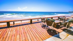 Une terrasse en bois avec des chaises et une table en osier, donnant sur l’océan.