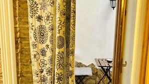 Uma entrada com cortina florida amarela que dá para uma área externa com mesa e banco.