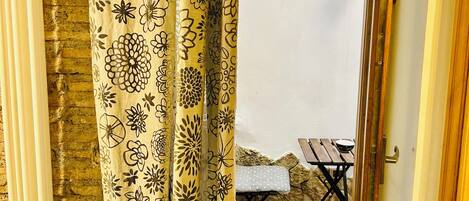 A doorway with a yellow floral curtain leading to an outdoor seating area with a table and bench.