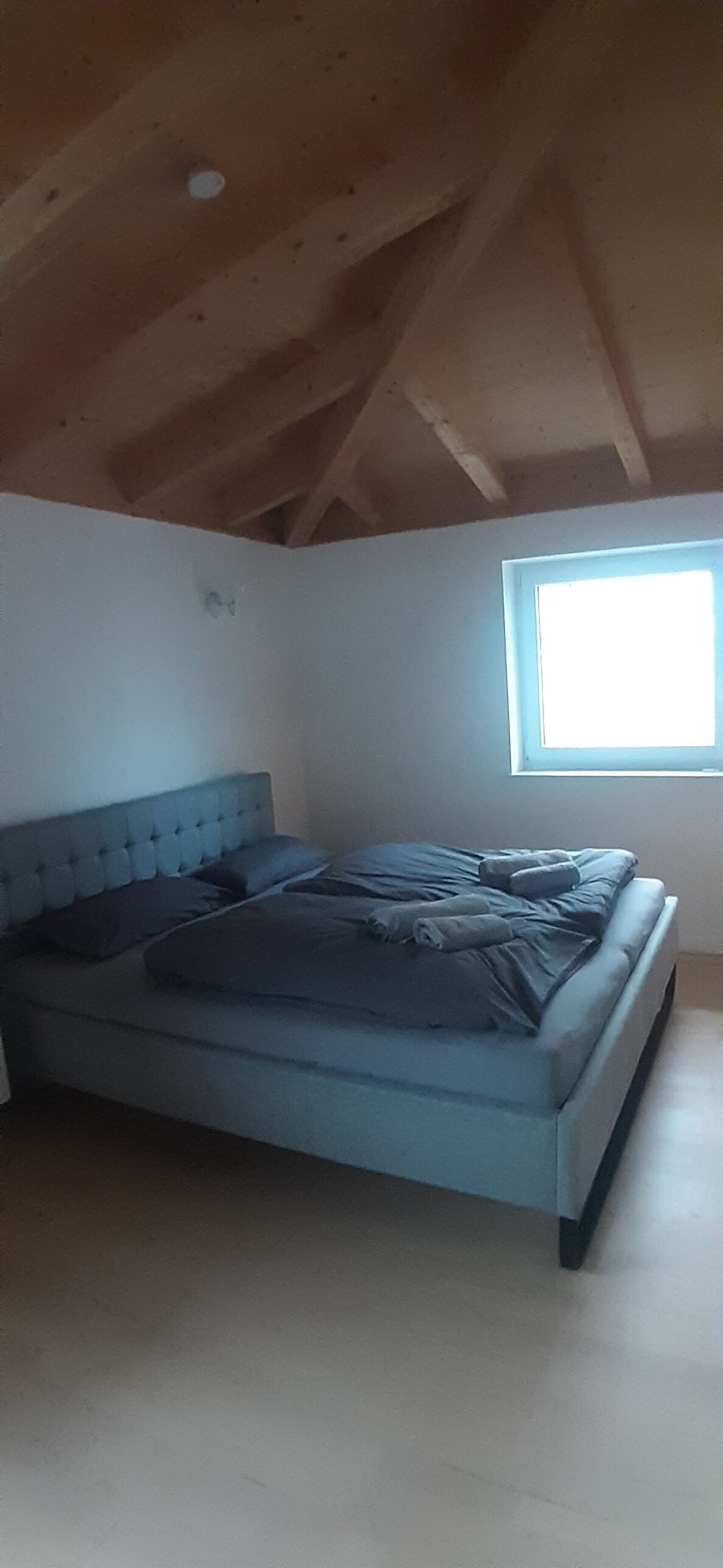 Un dormitorio con cama, ventana y vigas de madera en el techo.