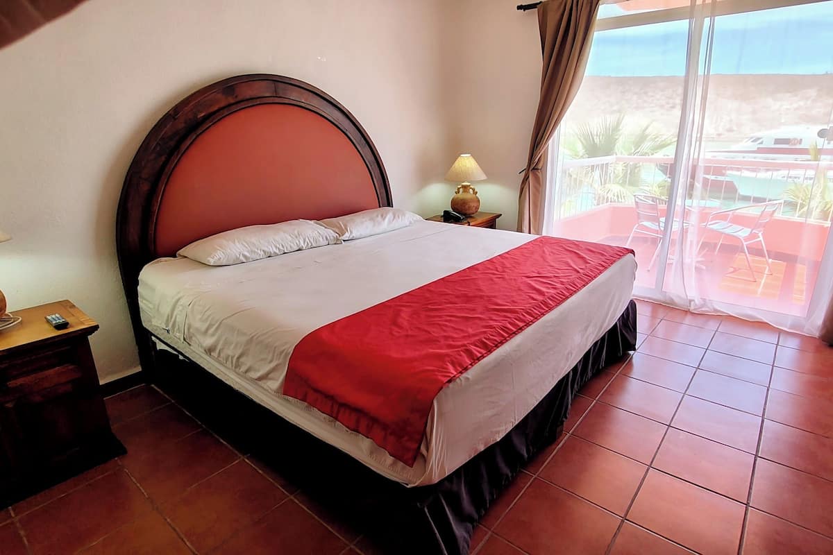 Habitación de hotel con cama, mesita de noche, lámpara y vistas al exterior.