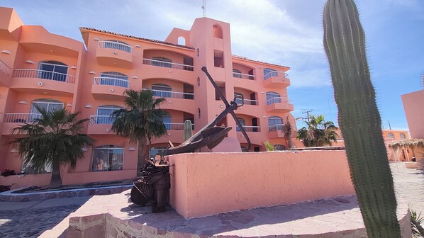 Un edificio de varios pisos con balcones, palmeras y un cactus.