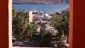 A coastal view through a window, featuring a clear sky, a calm sea, and a hilly landscape in the distance. - Club Hotel Cantamar Beach & Marina (Pichilingue)