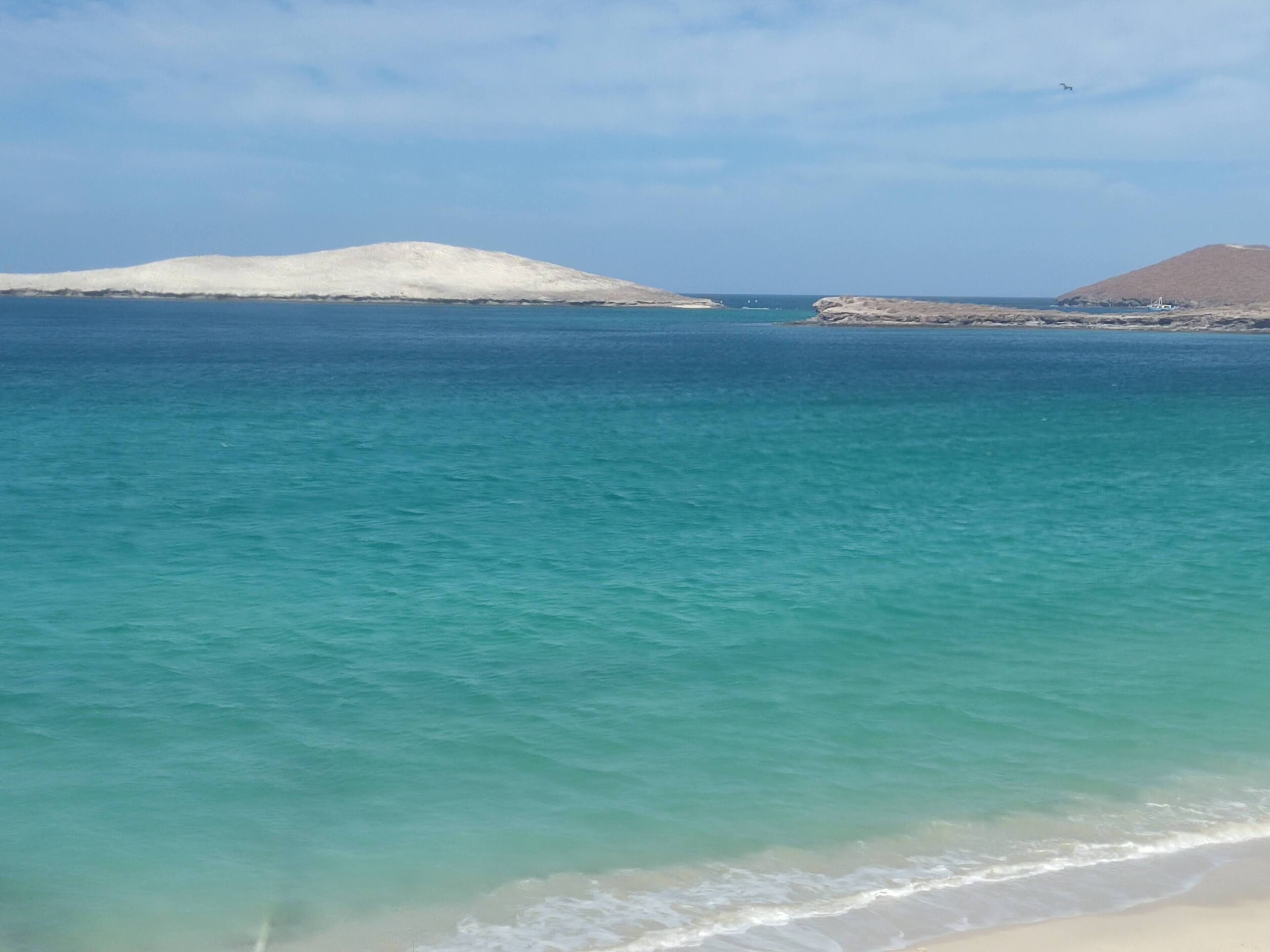 A coastal landscape with clear turquoise waters, sandy beach, and distant landforms.