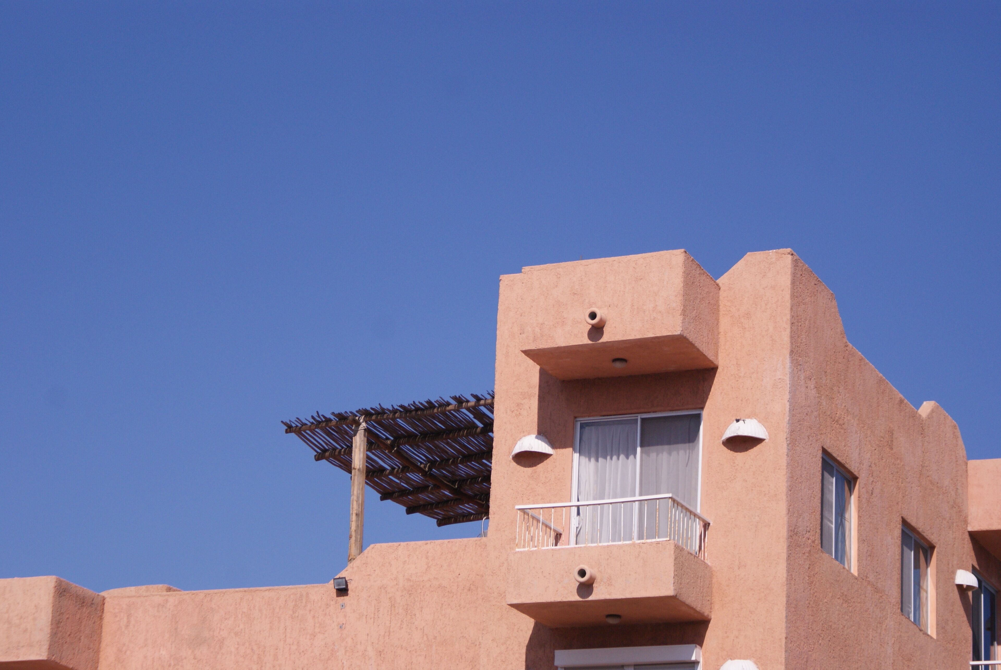 A building with a flat roof, a balcony with a railing, and a window with a curtain.