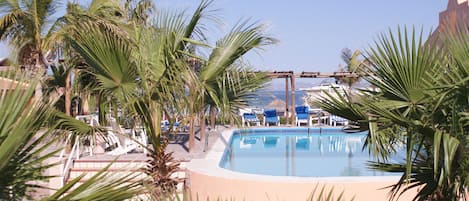 A pool surrounded by palm trees and lounge chairs.