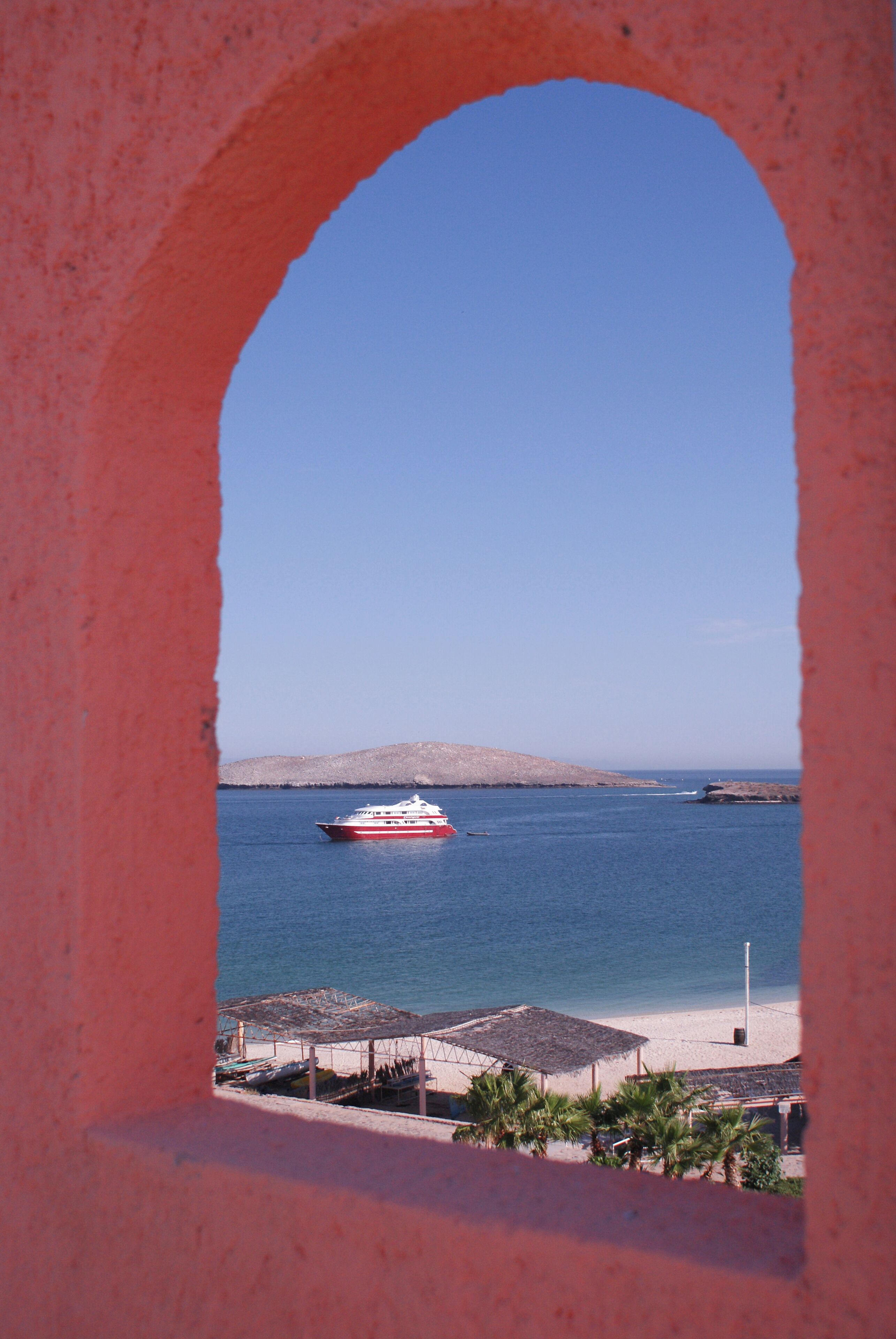 A view through an archway of a beach with a boat in the water and a distant hill.