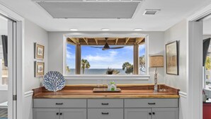 A kitchen with a wooden countertop, a large window with a view of the ocean, and a ceiling fan. - Port O' Call D203 - Direct Ocean View! Beach! (Isle of Palms)