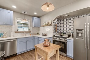 Una cucina moderna con mobili azzurri, un tavolo di legno, un bollitore in rame, una lavastoviglie in acciaio inossidabile, un forno integrato e un frigorifero.