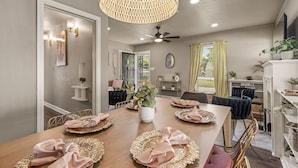 Un comedor con una mesa de madera dispuesta para cuatro personas, rodeada de sillas. Se observan un ventilador de techo e iluminación colgante sobre la mesa.