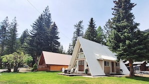 A two-story A-frame cabin with a porch, surrounded by a grassy yard and tall trees. - Cozy A-Frame Retreat w/ Views & Spacious Yard (Joseph)