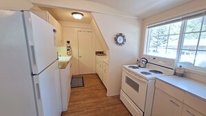 A kitchen with white appliances, a wooden floor, a window with a view, and a clock on the wall. - Cozy A-Frame Retreat w/ Views & Spacious Yard (Joseph)