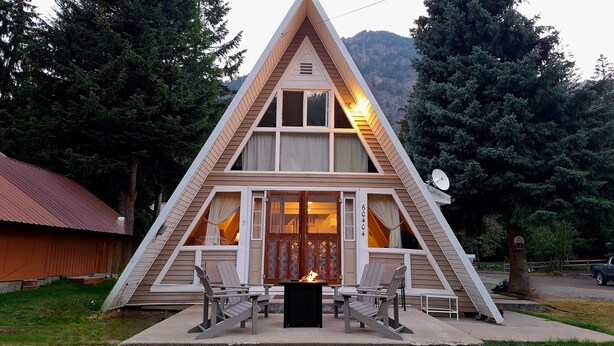 A triangular A-frame cabin with a fireplace, two chairs, and a table in front. - Cozy A-Frame Retreat w/ Views & Spacious Yard (Joseph)