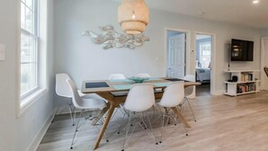 A dining area with a wooden table, white chairs, and a hanging light fixture.