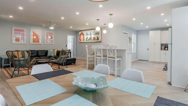 A modern living room with a sofa, chairs, a dining table, and a kitchen area in the background.
