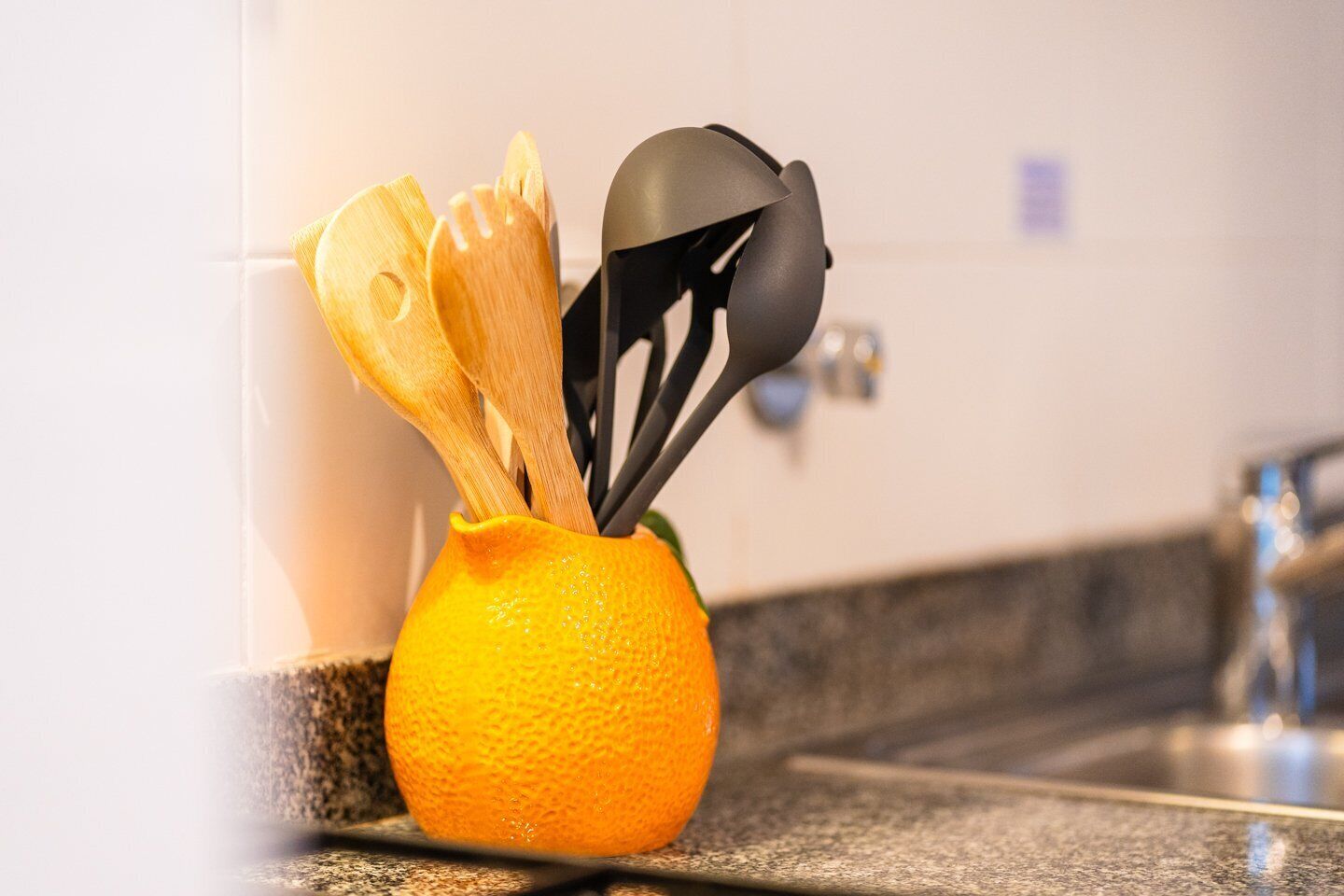 Una encimera de cocina con un utensilio para cucharas de madera que contiene una cuchara de madera y una espátula negra.