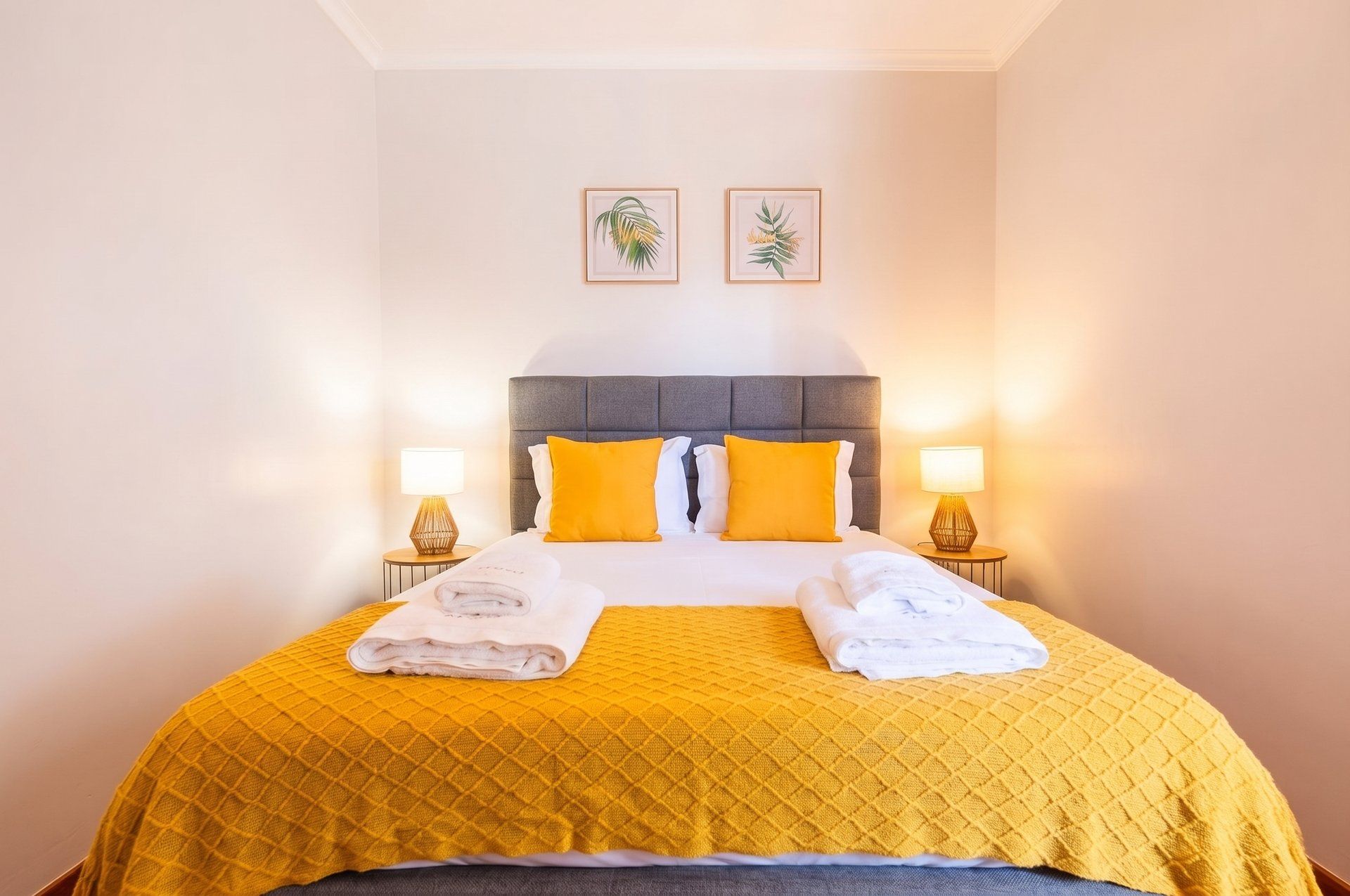Una camera d'albergo con un letto, due lampade ai comodini, una testiera e due quadri appesi al muro.