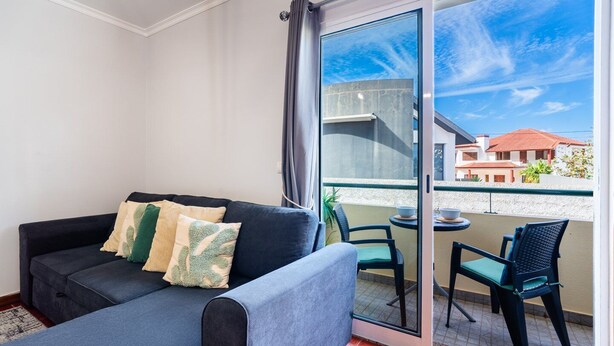 Ein Balkon mit einer Couch und Stühlen, einer Glastür und Blick auf Gebäude.