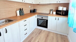 Une cuisine moderne avec des meubles en bois clair, un évier en acier inoxydable, un four encastré et un four à micro-ondes.